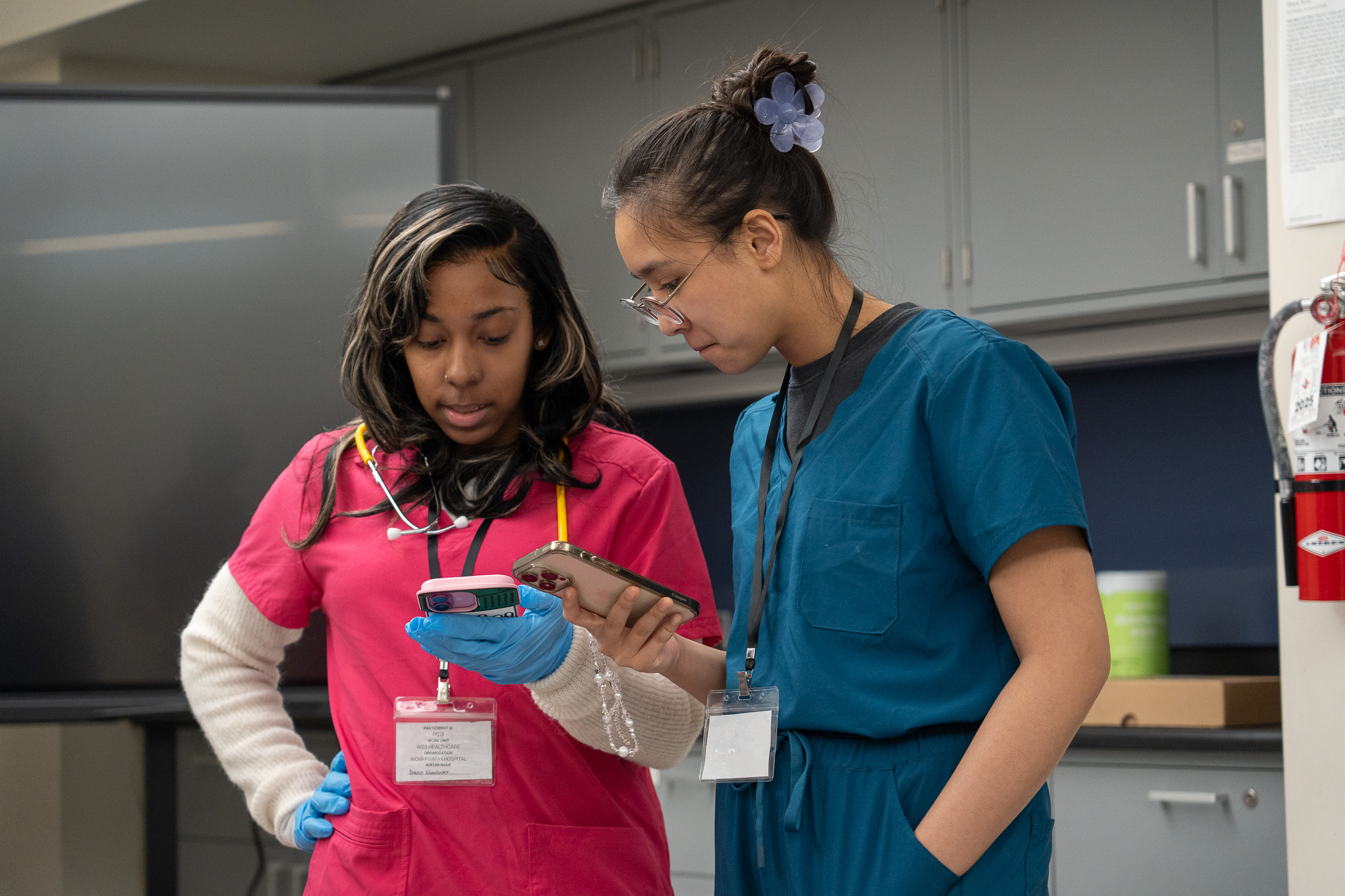 Two participants in scrubs checking their status in the app mid-simulation