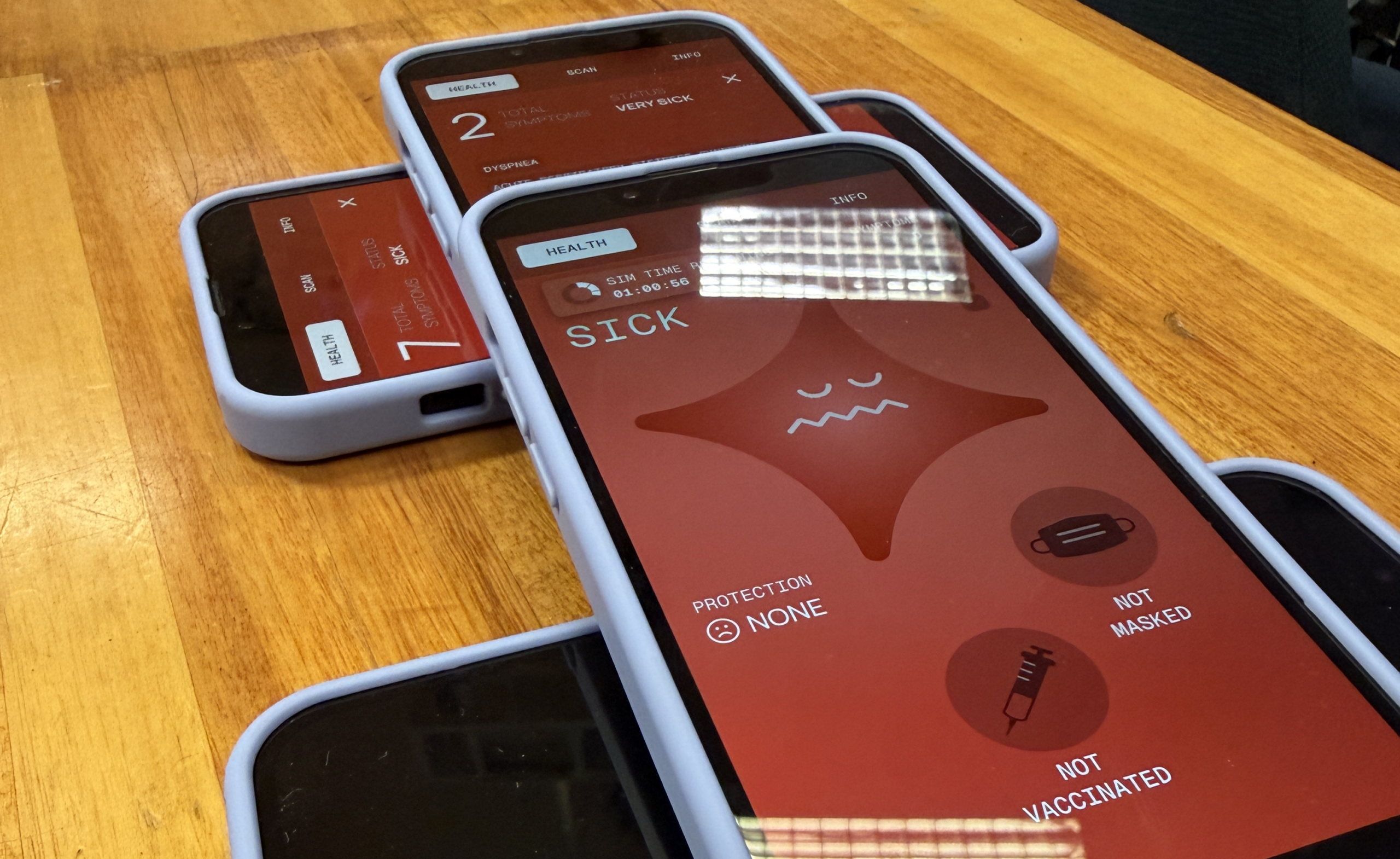 Participant phones on a table during the Cape Town exercise, showing sick and very sick health statuses with protection and vaccination state