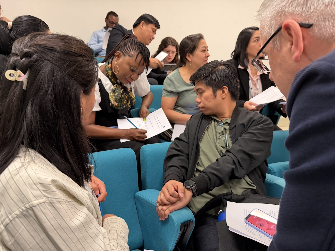 Participants at the Trieste training seated in discussion, working through printed injects with a phone showing an infected status in the foreground
